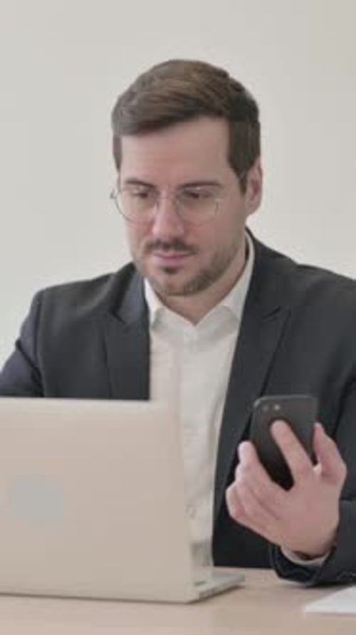 Man Using Laptop and Mobile Phone in Office