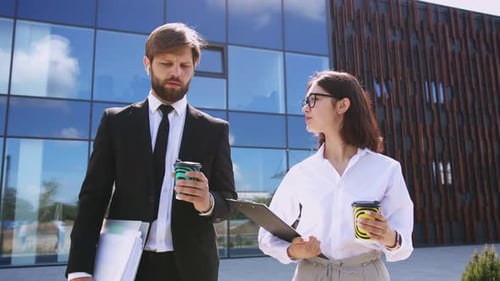 Caucasian Business Colleagues in Formal Clothes Walking on Street and Discussing Some Working Issues
