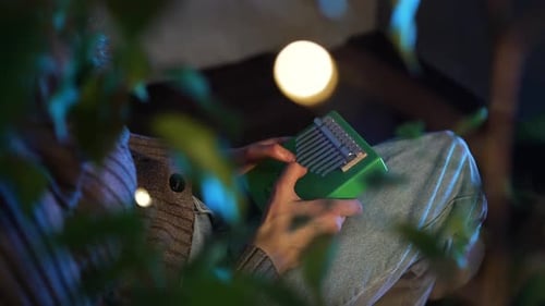 Female Musician Performing Green Kalimba Relaxing Near Houseplants with Soft Illumination Generating