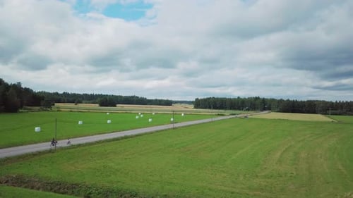People cycle down empty road in green countryside, aerial drone shot