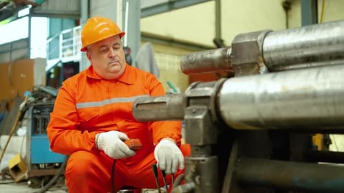 Leitender Wirtschaftsingenieur in Sicherheitsuniform, der schwere Maschinenrollen mit einer Fernbedienung bedient