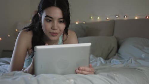 Woman Relaxes on Bed Using a Tablet Device