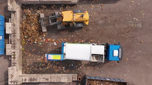 Food waste dumped by truck and wheel loader pushes it onto heap, top-down aerial