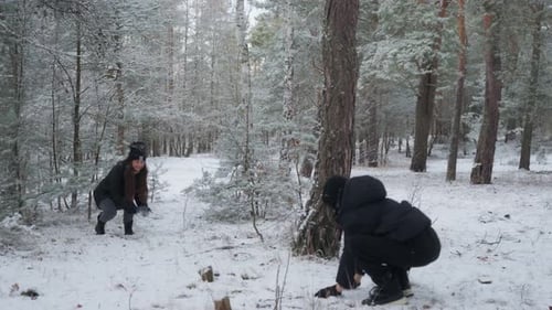 Mother and son having a fun snowball fight in a snowy winter forest.