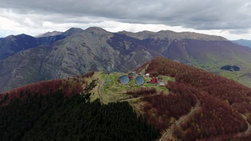 Abandoned radar facility on a forested mountain ridge under dramatic cloudy sky