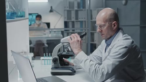 Scientist Working with Microscope and Laptop in Lab