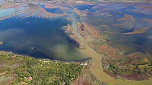 Lagoon with land surrounded by mud and shallow water, bordered by a sandy beach and trees from the A