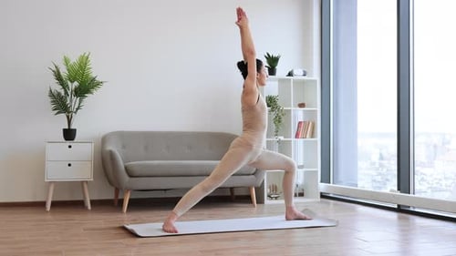 Reife Brünette praktiziert Warrior I Halfway Fold während der Yoga-Übung zu Hause