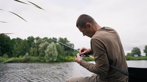 Fisherman with fishing rod or spinning and professional tools sitting on the river bank rear