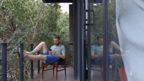 White caucasian male man with beard relaxing on hotel balcony on his phone