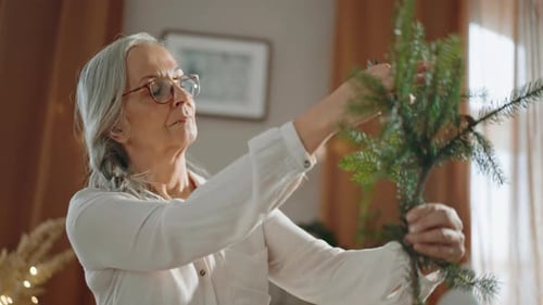 Senior Woman Arranging Christmas Tree Branches Indoors