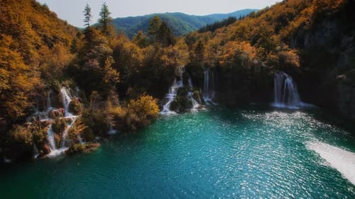 Arroyo en cascada que cae por las rocas del bosque de montaña con árboles amarillentos y caídas de color naranja brillante