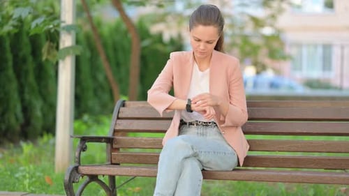 Woman Checking Smartwatch While Waiting on Park Bench