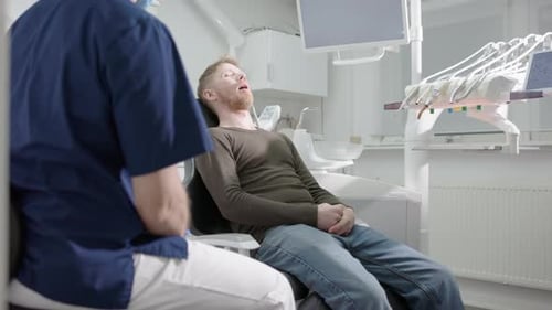 Dentist speaking to male dental patient sitting in reclined chair of clinic