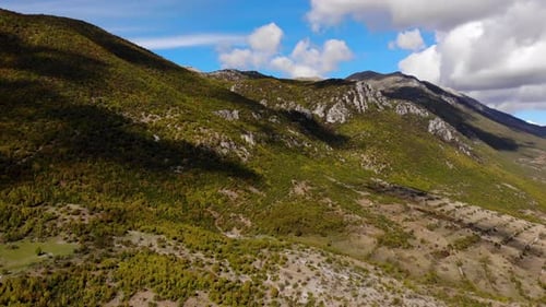 Paradise mountain scenery with rocky slopes and forests under white clouds on blue sky