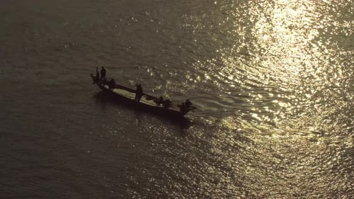 Plan aérien d'un bateau de pêche partant au coucher du soleil avec des gens agitant leur silhouette sous le soleil du soir