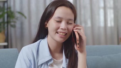 Close Up Of Asian Teen Girl Talking On Smartphone While Sitting On Sofa In The Living Room