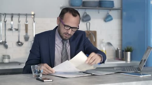 Man in suit reviewing documents at kitchen counter