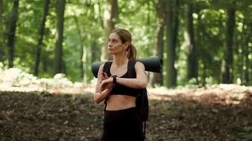 Woman With Backpack Checks Watch While Hiking in a Forested Area During Daylight Hours
