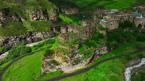 Ancient Ruins of Cliffside Stone Buildings Above Lively River in Breathtaking Green Valley
