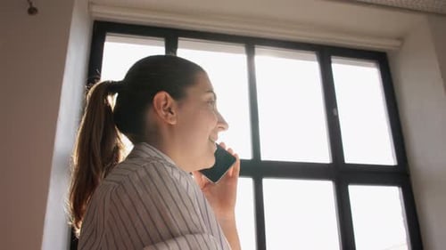 Woman Talks on Phone in Bright, Sunny Window