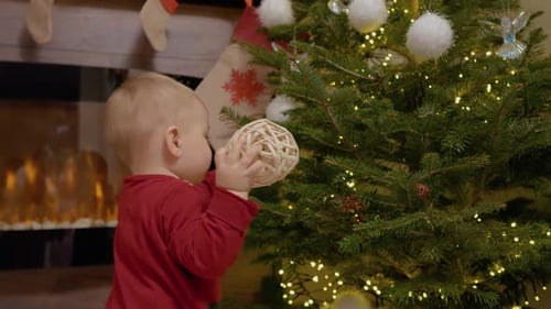 Infant with Christmas Ornament Near Decorated Christmas Tree