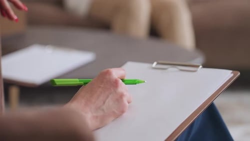 Thérapeute écrivant à la main avec un stylo vert sur le presse-papiers pendant la session avec le client