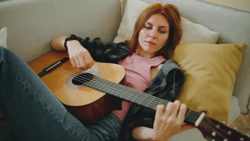 Woman Playing Guitar on Sofa at Home