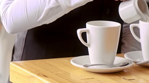 Woman pouring cream into coffee mugs preparing drinks for cafe customers