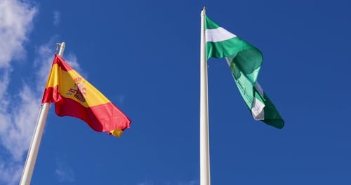 Spanish and Andalusian Flags Waving Against Blue Sky