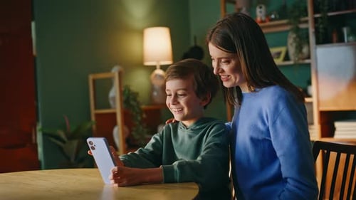Smiling Boy and Woman Looking at Smartphone Indoors