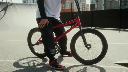 BMX Rider Resting at Skate Park with Another Cyclist Training in Background