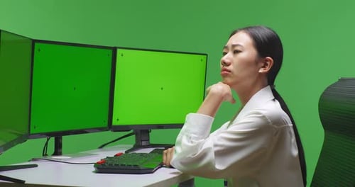Asian Woman Thinking While Working With Mock Up Multiple Computer Monitor In Green Screen Studio