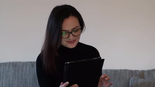 Woman Uses Tablet While Relaxing on Gray Couch