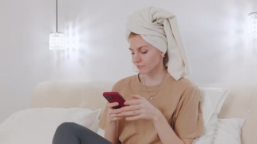 Woman Using Phone on Bed with Towel on Head