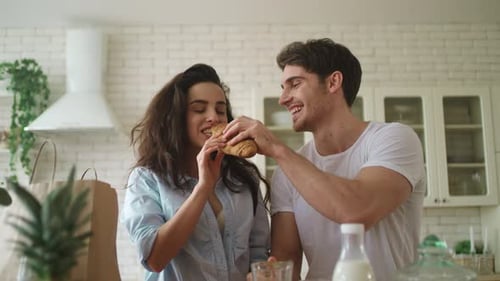 Couple shares croissant in bright kitchen, morning routine
