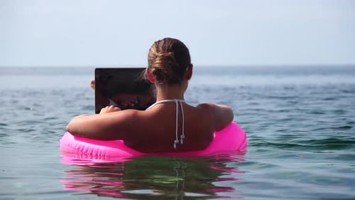 Woman Freelancer Works on Laptop Swimming in Sea on Pink Inflatable Ring Happy Tourist in Sunglases