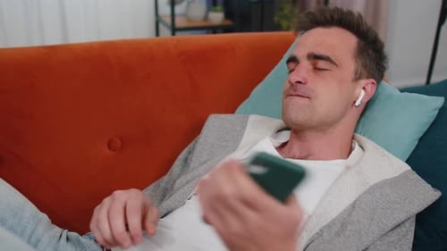 Man Listening to Music on Couch with Earbuds