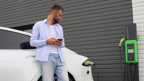 Man Using Phone While Charging Electric Car