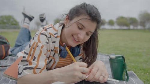 Pretty Girl Lying on Green Grass in Park and Taking Notes in Copybook