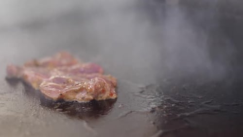 Placing raw meat and cheese slices on hot iron cooktop. Close up, slow motion