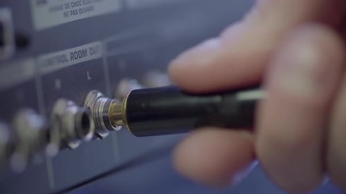 Audio engineer plugs in quarter inch stereo audio cables into mixer. Left and right channels plugged