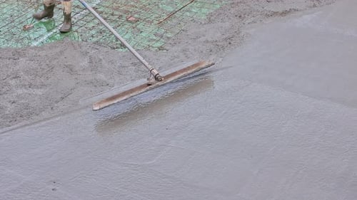 Worker Levels Fresh Concrete on Construction Site Building in Progress