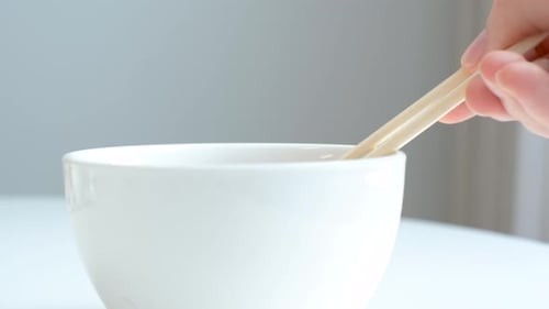 Wooden chopsticks holding japanese natto beans on gray background front view.