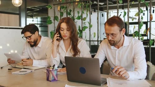 Trois collègues collaborent dans un espace de bureau, une femme d'affaires parle au téléphone tandis que d'autres