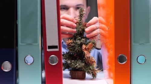 An Office Worker Decorates a Shelf with Archive Folders Small Christmas Tree