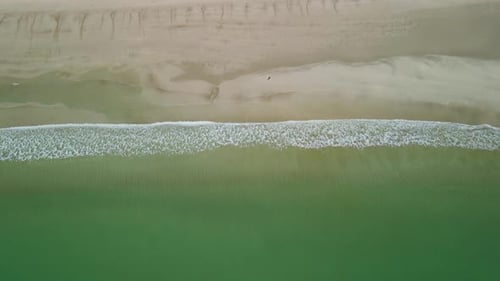 Wellen brechen ruhig an Land, während die Person am Strand entlang geht. Immer noch Drohnenaufnahmen aus der Luft von oben.