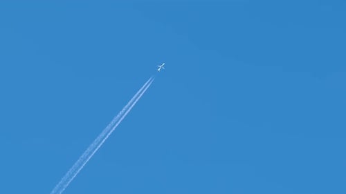 Commercial Airplane Ascending with Long Contrail in Blue Sky