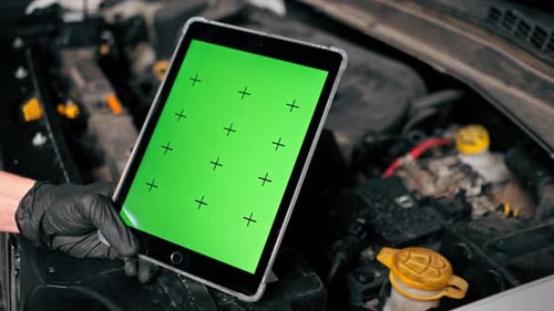 Close-up of a hand with a tablet on which the green screen is open against the background of a car