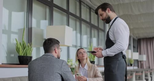 Waiter Takes an Order From a Young Couple in Restaurant Cafe Worker Taking Note Writing Order